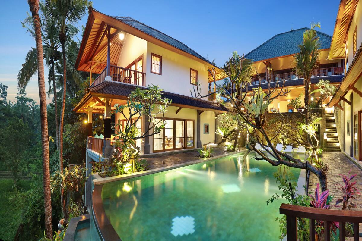 A large house with a swimming pool, surrounded by lush greenery and palm trees.