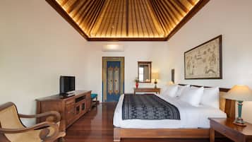 Een slaapkamer met een houten plafond, een bed met wit beddengoed, een houten nachtkastje, een stoel en een televisie op een houten kast.