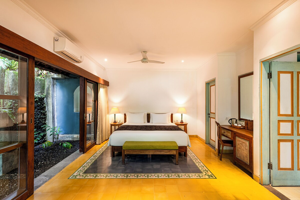 A hotel room with a bed, bedside tables, a ceiling fan, and a view of the outdoors.
