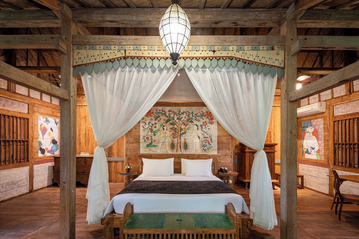 A room with a bed, a canopy, a wooden ceiling, and a wall painting.