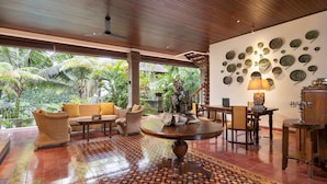 A spacious living area with a large round table, comfortable seating, and a view of lush greenery outside. - Korurua Dijiwa Ubud (Ubud)