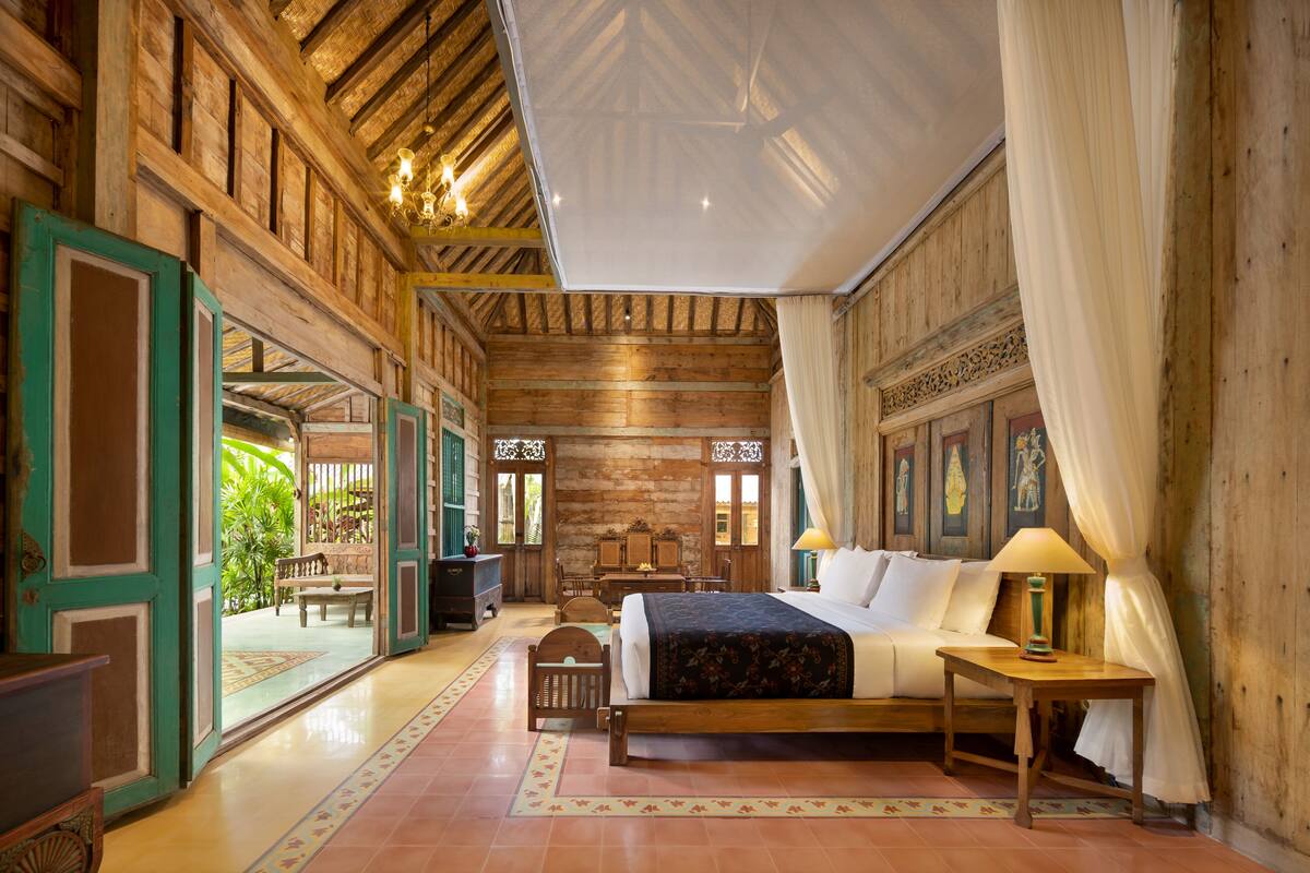 A spacious room with a large bed, wooden ceiling, and a view of a garden.
