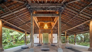 A covered outdoor area with wooden beams and pillars, a central chandelier, and yoga mats on the floor. - Korurua Dijiwa Ubud (Ubud)