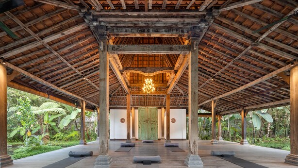 A covered outdoor area with wooden beams and pillars, a central chandelier, and yoga mats on the floor. - Korurua Dijiwa Ubud (Ubud)