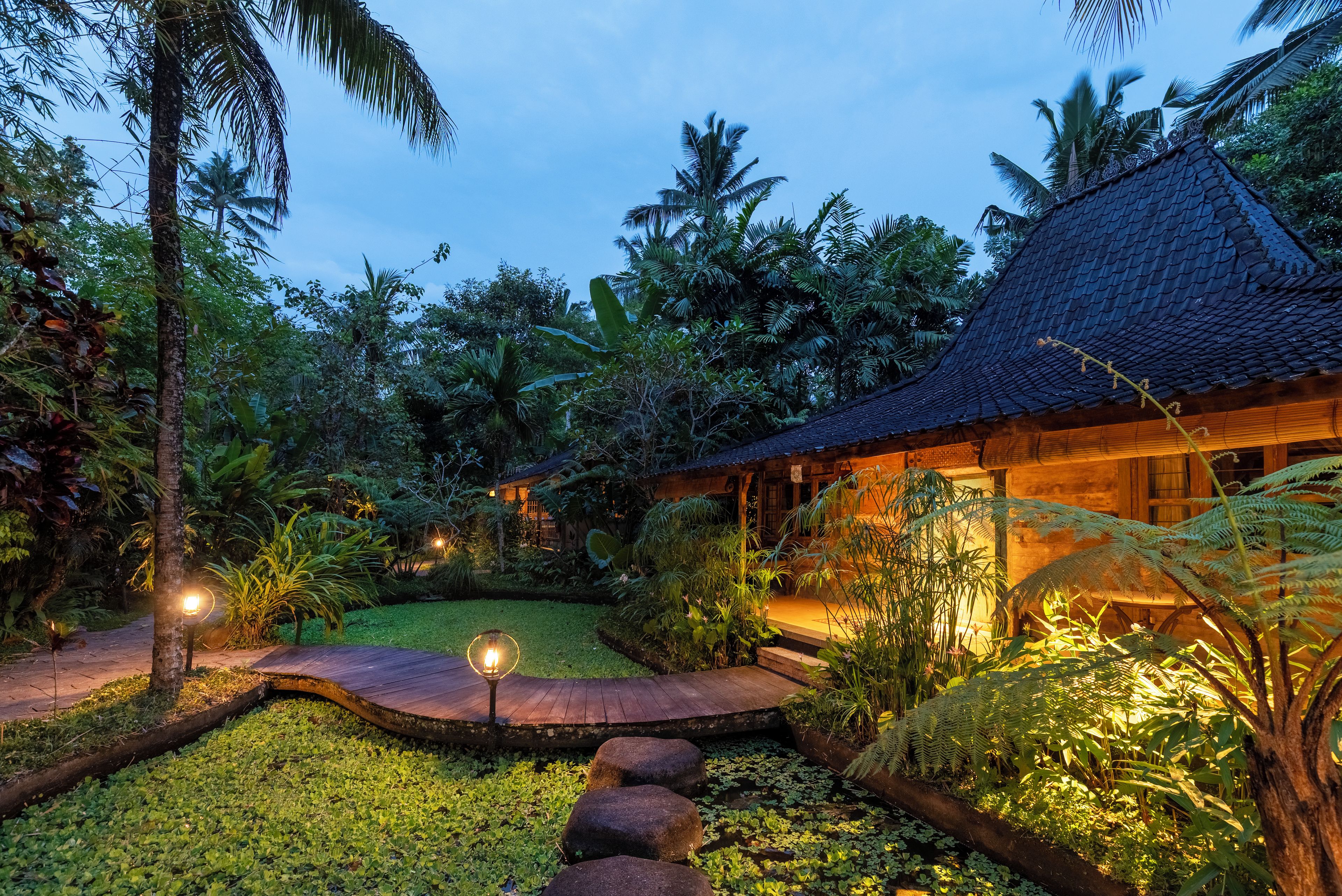 Un complexe hôtelier tropical doté d’une maison en bois, d’un jardin avec des nénuphars et d’un sentier menant à la maison.