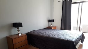 Ein Schlafzimmer mit einem Bett, zwei Nachttischen, einer Kommode und einem Fenster mit Vorhängen.