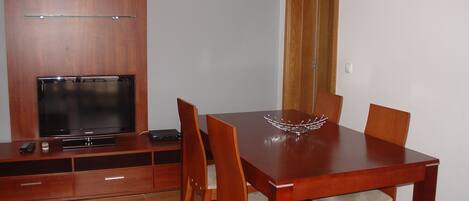 A dining area with a wooden table and chairs, a television on a wooden cabinet, and a door in the background.