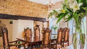 A dining area with a stone wall, wooden chairs with floral upholstery, and a vase with flowers on a table.