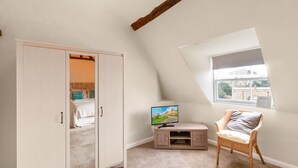 A bedroom with a sloped ceiling, a wardrobe, a television, a chair, and a window.