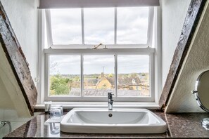 Un baño con lavamanos blanco, una ventana y vistas a casas.