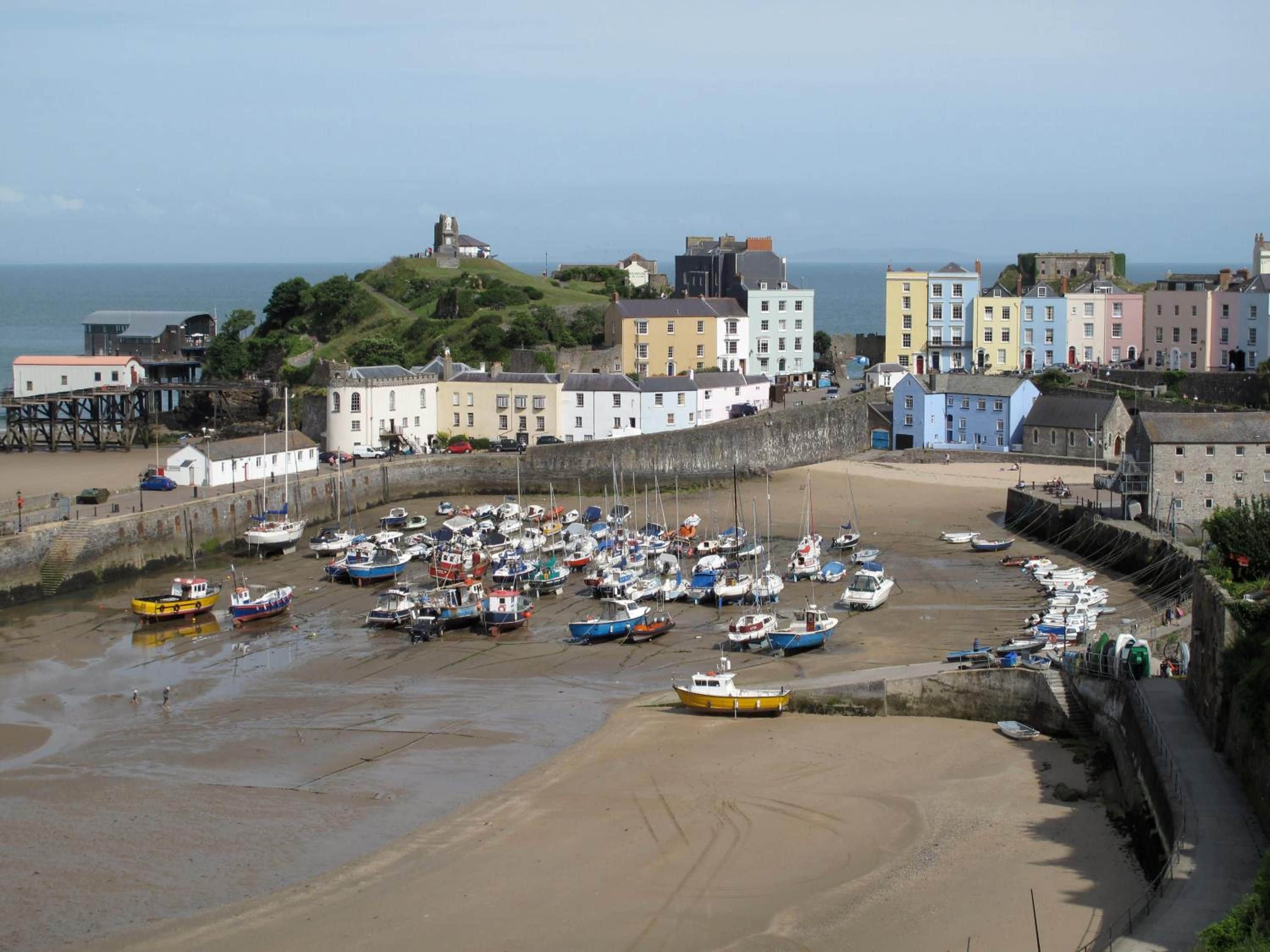 A coastal town with a sandy beach, a stone wall, and colorful buildings.
