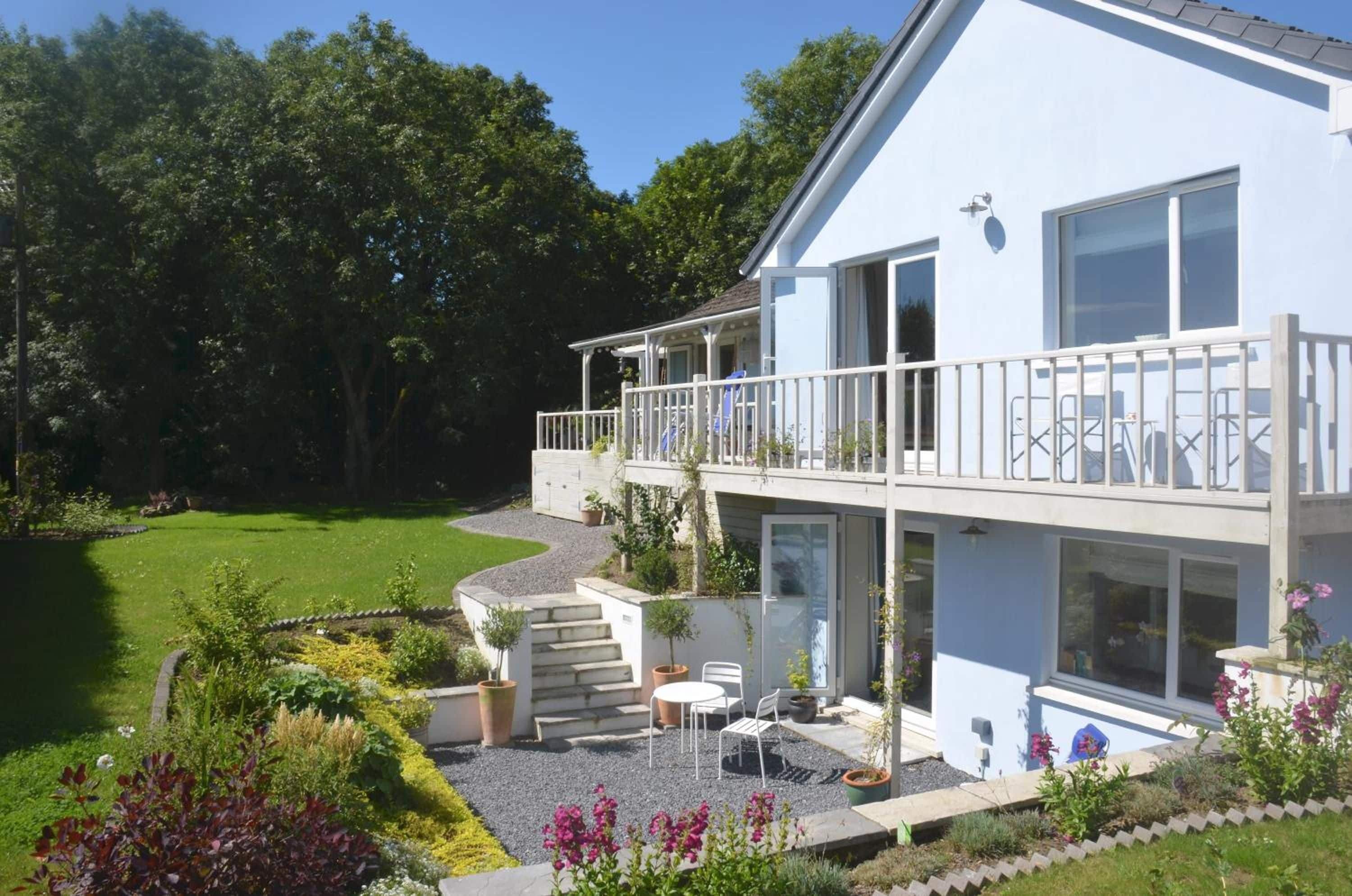 Une maison à deux étages avec un balcon, un petit patio doté de mobilier d’extérieur et un jardin bien entretenu.