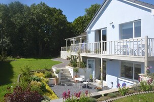 Una casa de dos pisos con un balcón, un pequeño patio con mobiliario exterior y un jardín bien cuidado.