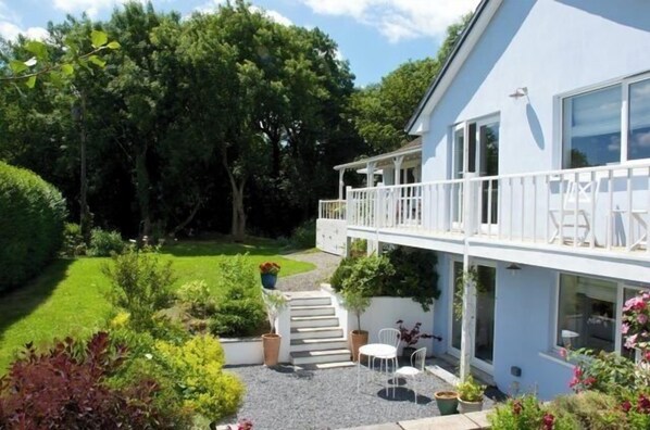 A two-story house with a balcony, a garden, and a pathway leading to the entrance.