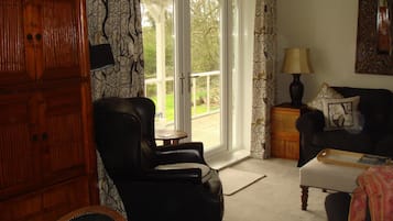 Uma sala de estar com uma poltrona de couro preto, um armário de madeira, um sofá e uma mesa com abajur.