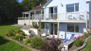 A two-story house with a balcony, a small patio with a table and chairs, and a garden area with various plants. - Gower View Luxury bed & Breakfast (Tenby)
