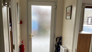 Un pasillo con puerta de vidrio satinado, extintor, radiador y felpudo en la entrada.