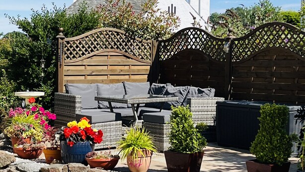 Un jardín con un portón de madera, plantas en macetas y mobiliario de exterior.