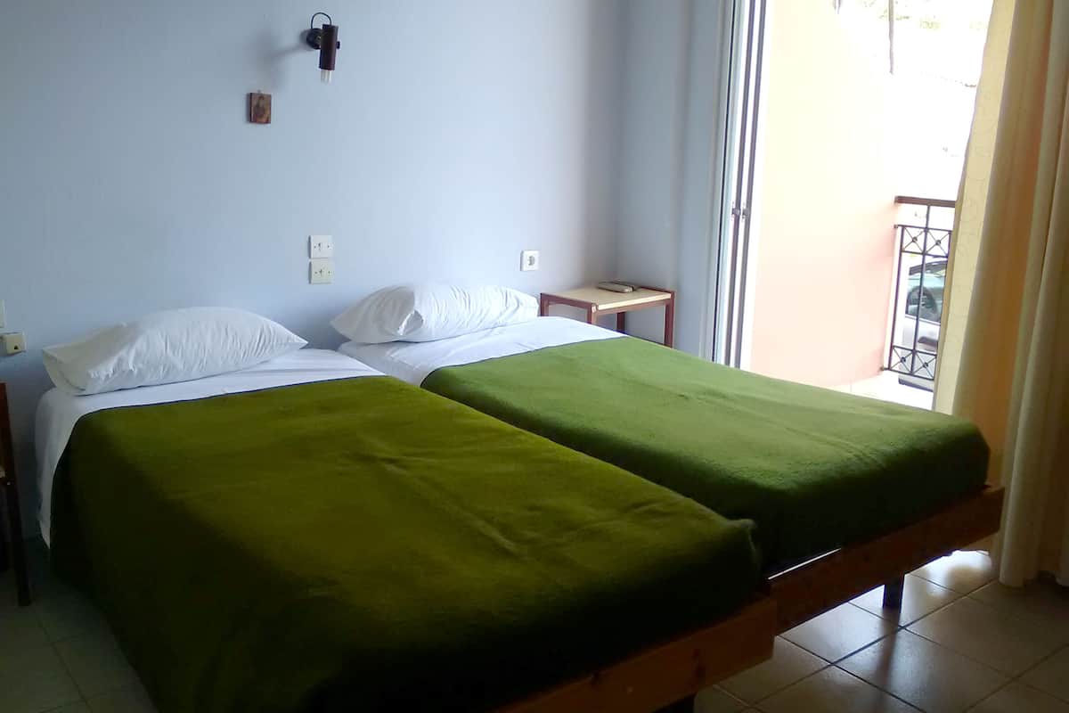 Ein Zimmer mit zwei Betten, jedes mit einer grünen Tagesdecke, weißen Kissen und einem kleinen Nachttisch mit einer Lampe.