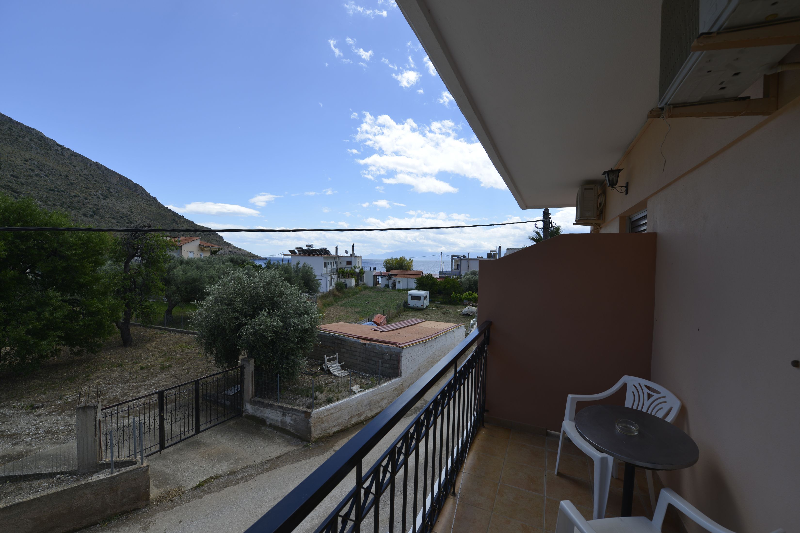A balcony with a view of a hillside, a white chair, and a small table.