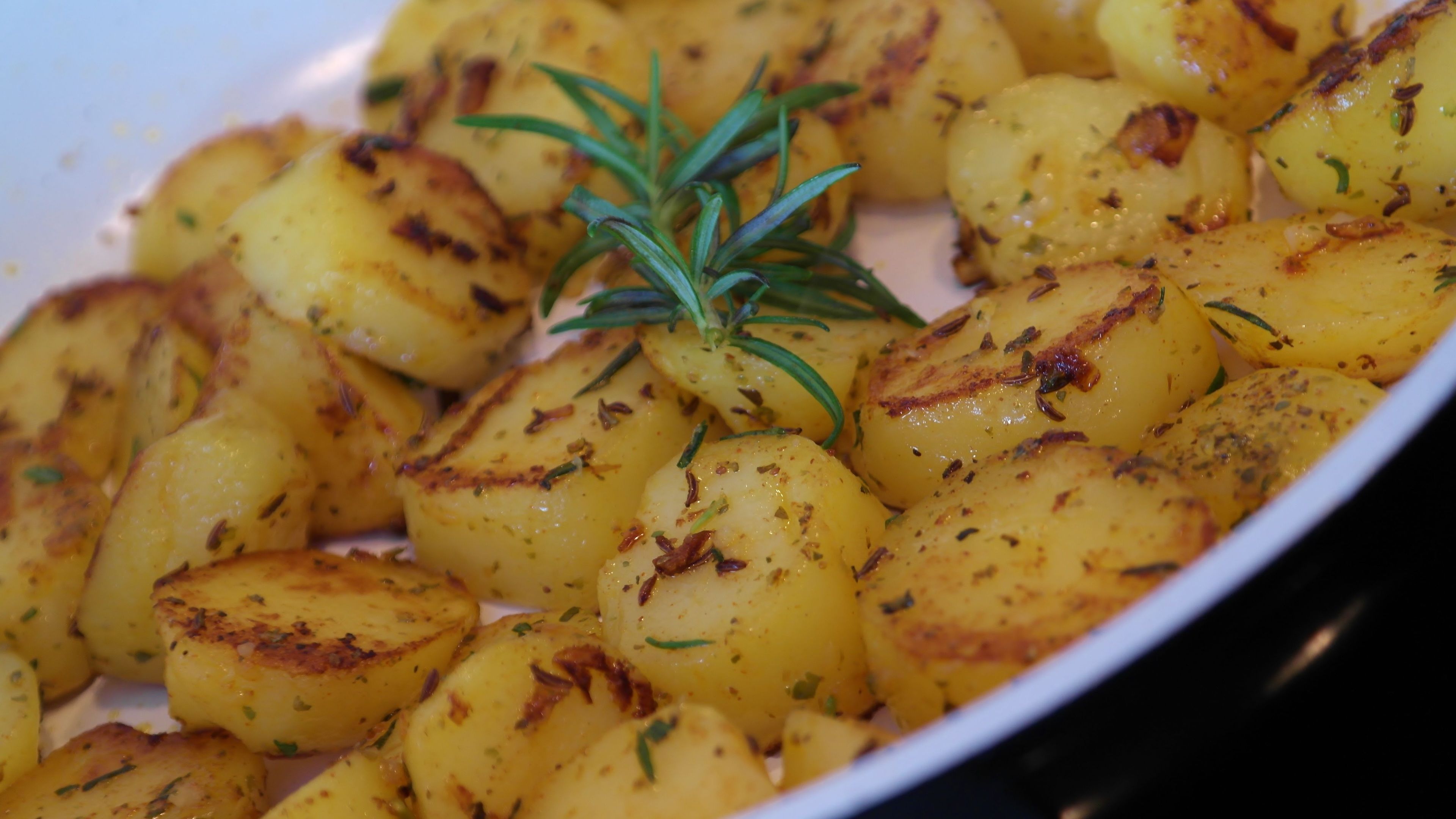 A close-up of roasted potatoes seasoned with herbs and a sprig of rosemary.