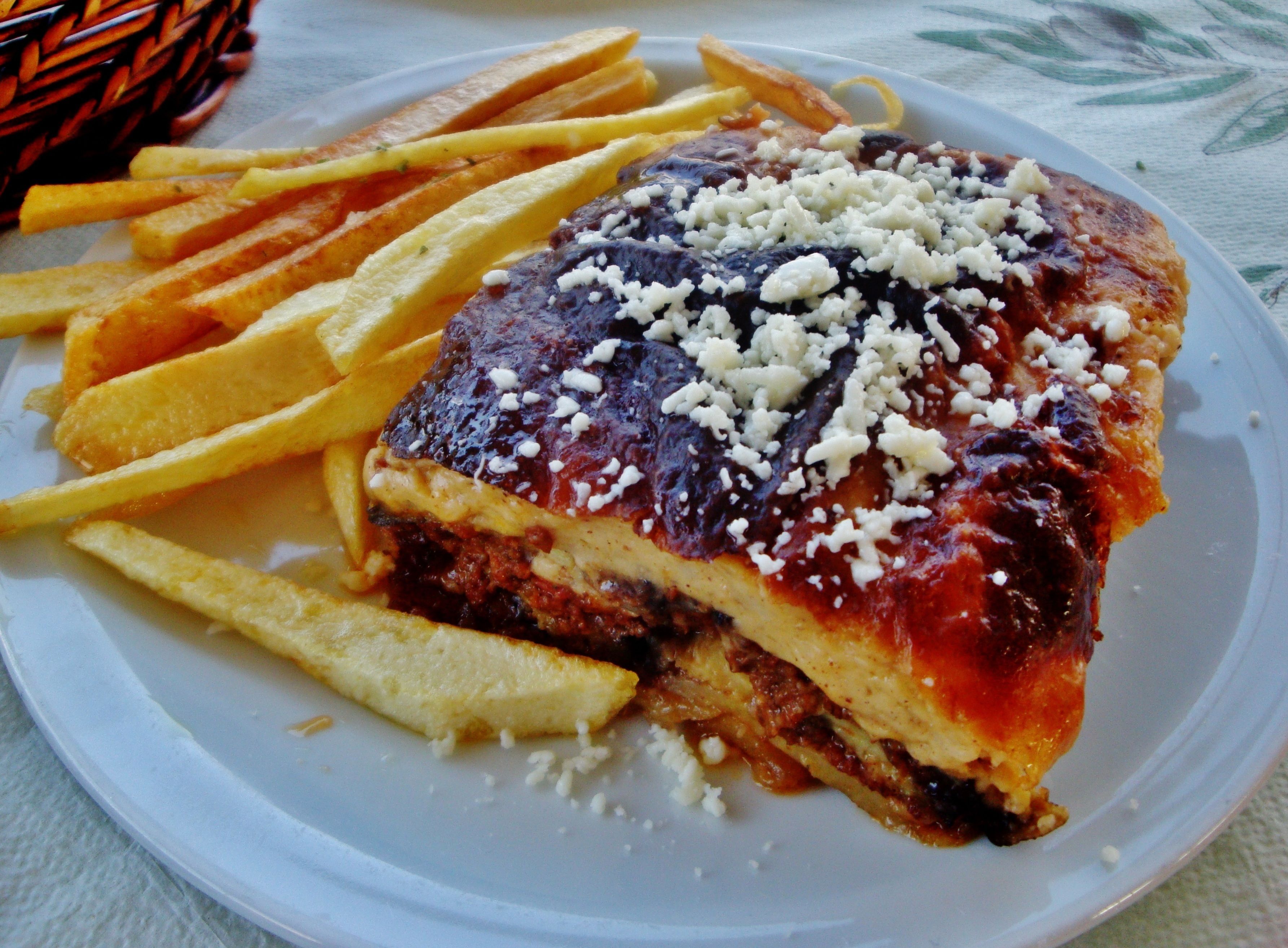 Een bord met een plak lasagna, frieten en een klein mandje.