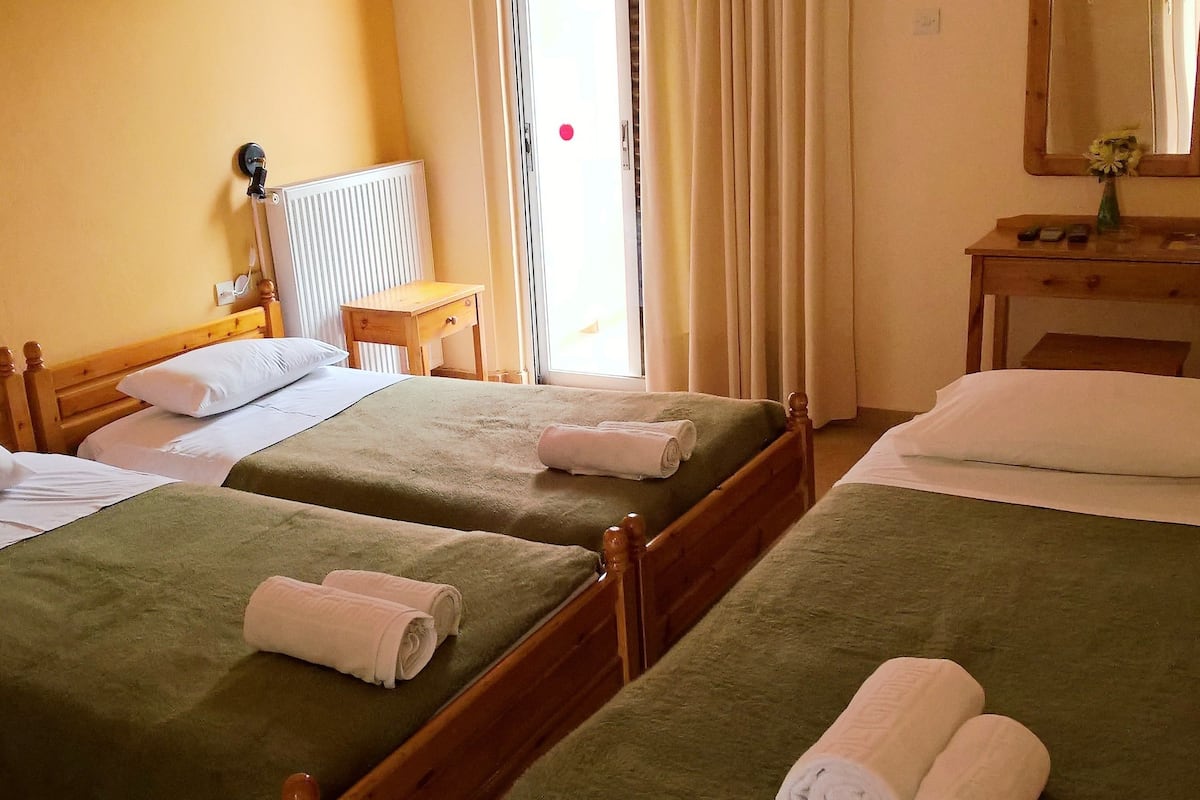 Ein Hotelzimmer mit zwei Einzelbetten, einem Holfnachtkästchen, einem kleinen Tisch und einem Spiegel an der Wand.