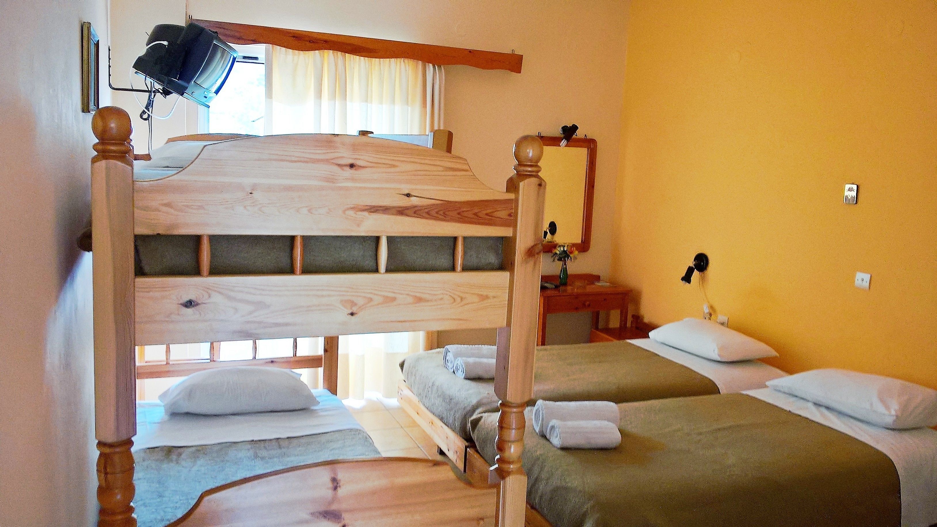 Ein Zimmer mit einem Etagenbett, zwei Einzelbetten, einem Schreibtisch mit Stuhl, einem Spiegel und einem fenster mit Vorhängen.