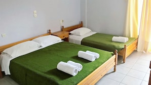Habitación de hotel con dos camas individuales, cada una con cubrecama verde y almohadas blancas. Hay dos toallas enrolladas en cada cama.