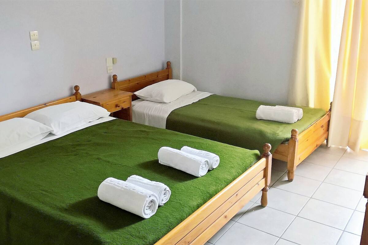 Ein Hotelzimmer mit zwei Einzelbetten, jedes mit einer grünen Tagesdecke und weißen Kissen. Auf jedem Bett liegen zwei zusammengerollte Handtücher.