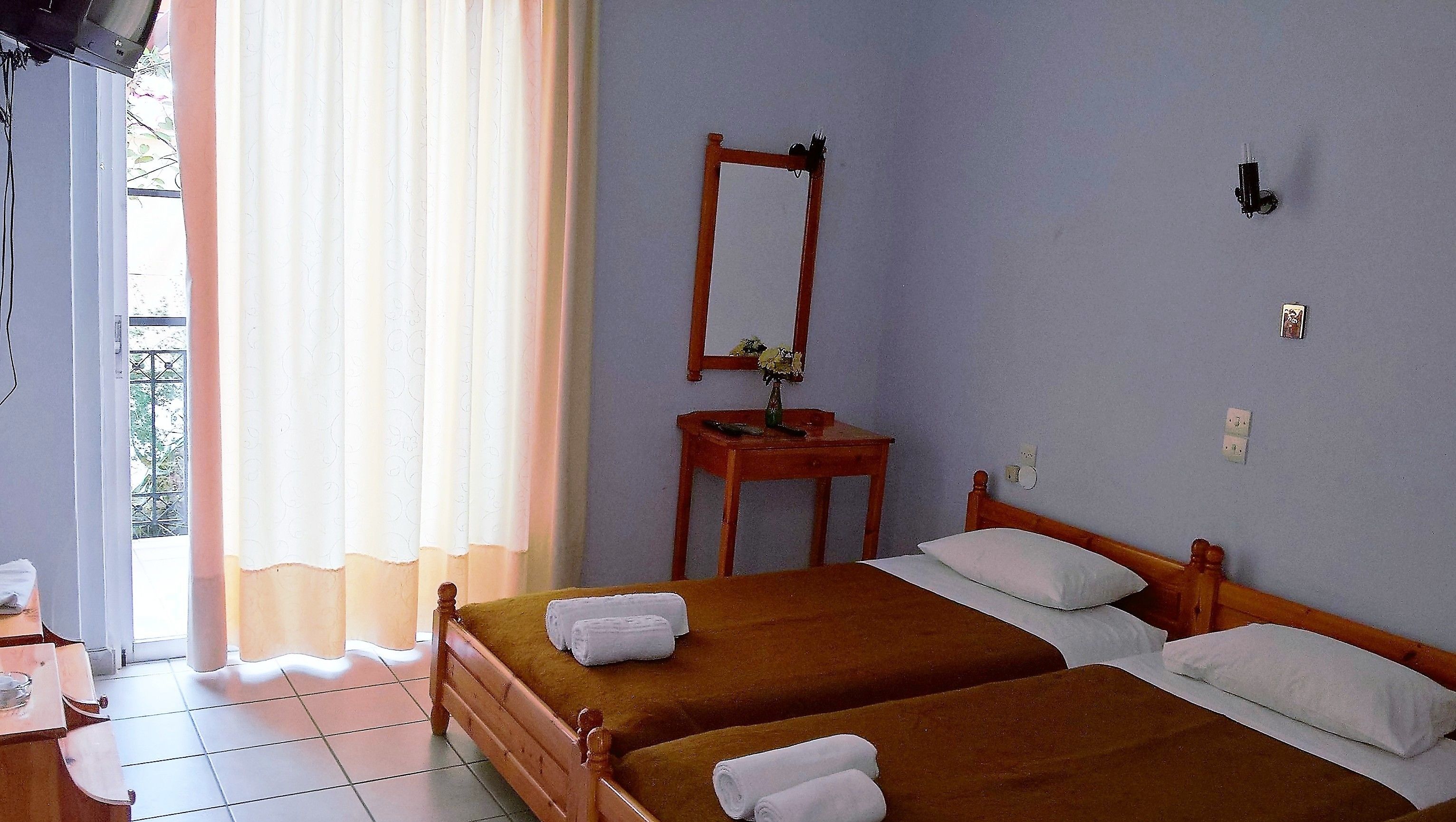 A room with two wooden beds, a wooden nightstand with a vase, a mirror, and a window with curtains.