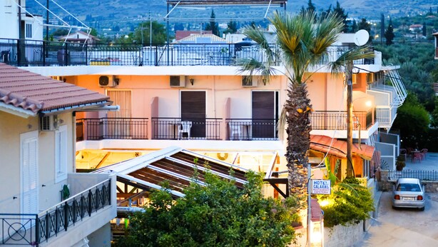 Un hotel con balcón, una palmera y un cartel que indica que es hotel y restaurante.