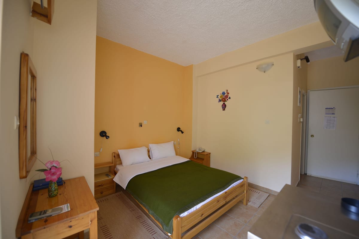 Ein Schlafzimmer mit einem Bett, einem Nachttisch und einem kleinen Schreibtisch mit Blumen in einer Vase.