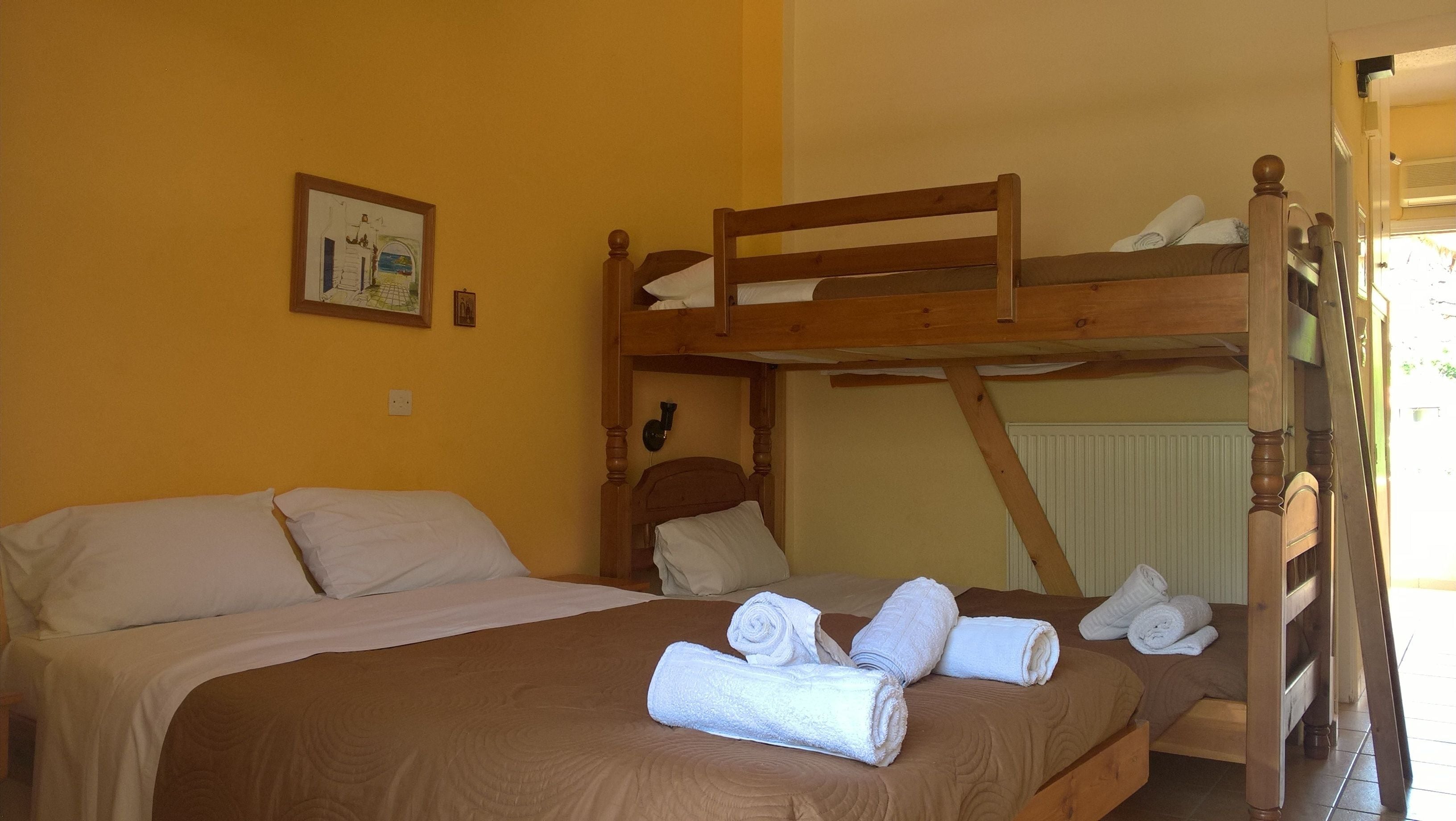 Une chambre avec un lit superposé, une couette marron, un lit simple et un tableau encadré au mur.