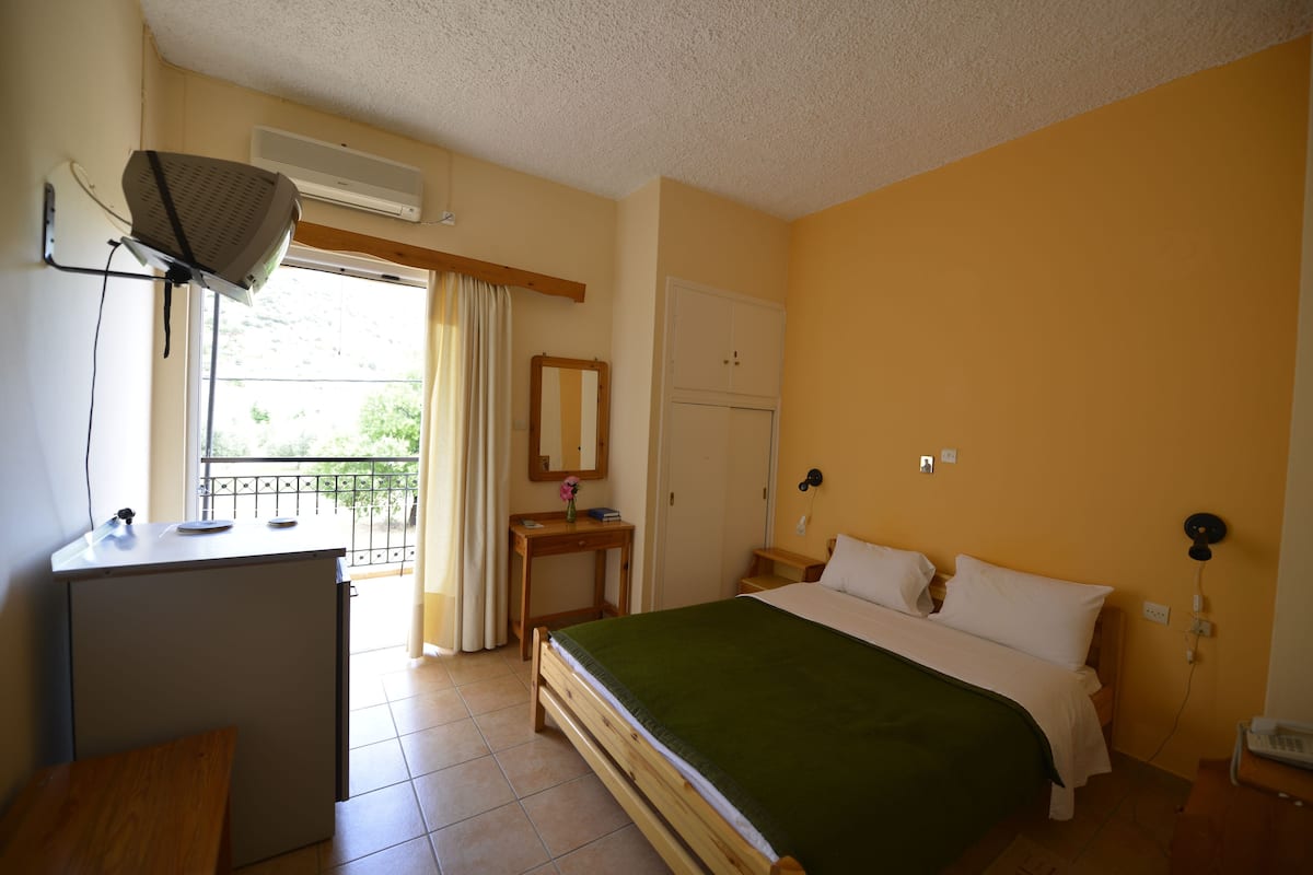 Ein Schlafzimmer mit Bett, Schreibtisch, Stuhl, Spiegel, Kleiderschrank und einem Fenster mit Vorhängen.
