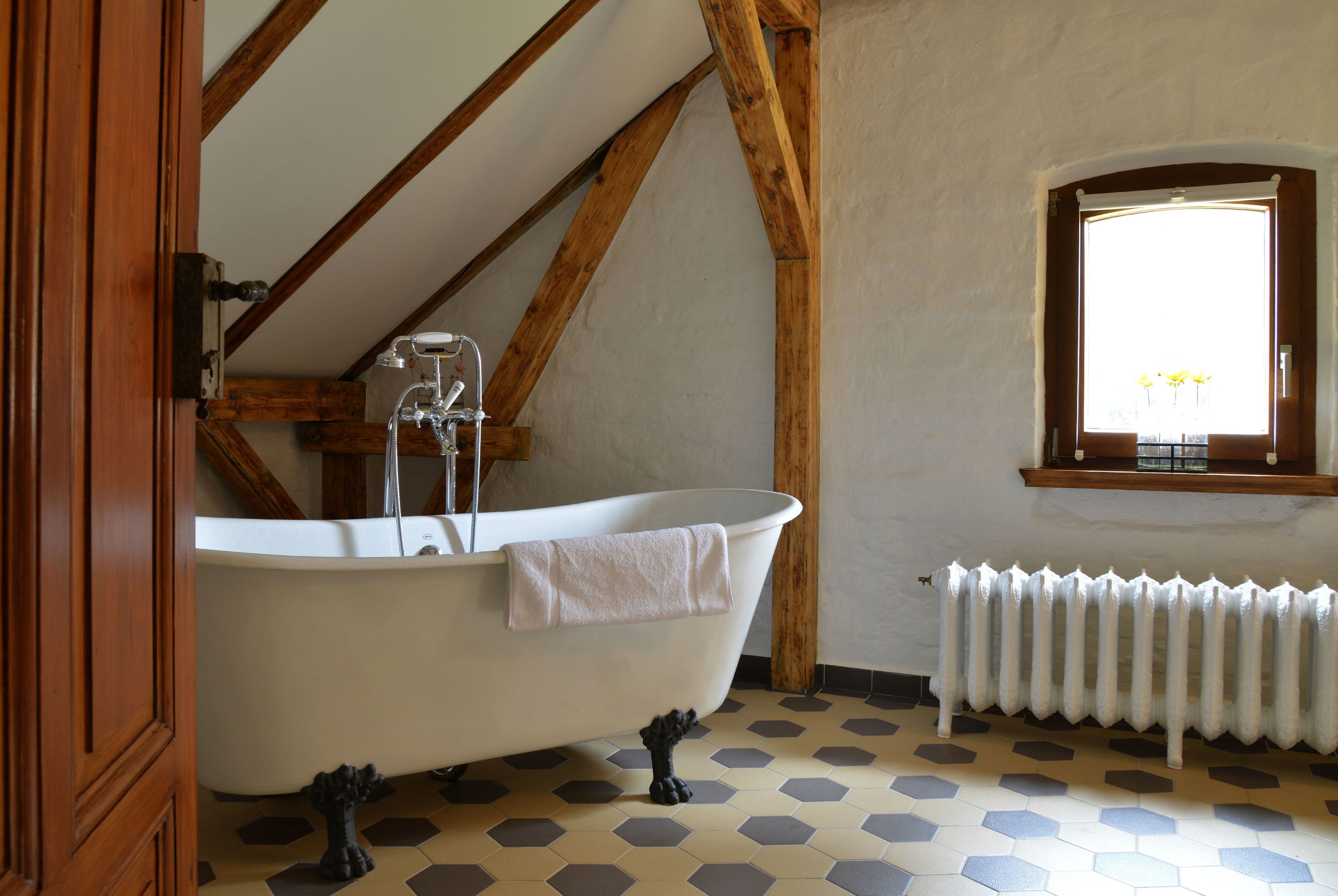 Un baño con una bañera independiente, vigas de madera, un radiador y una ventana con vistas.