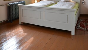 Quarto com uma cama de solteiro, radiador, janela e luminária suspensa.