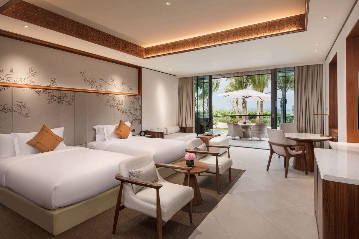 Une chambre d’hôtel avec deux lits, un coin salon avec une table et des chaises, et une vue sur l’extérieur.