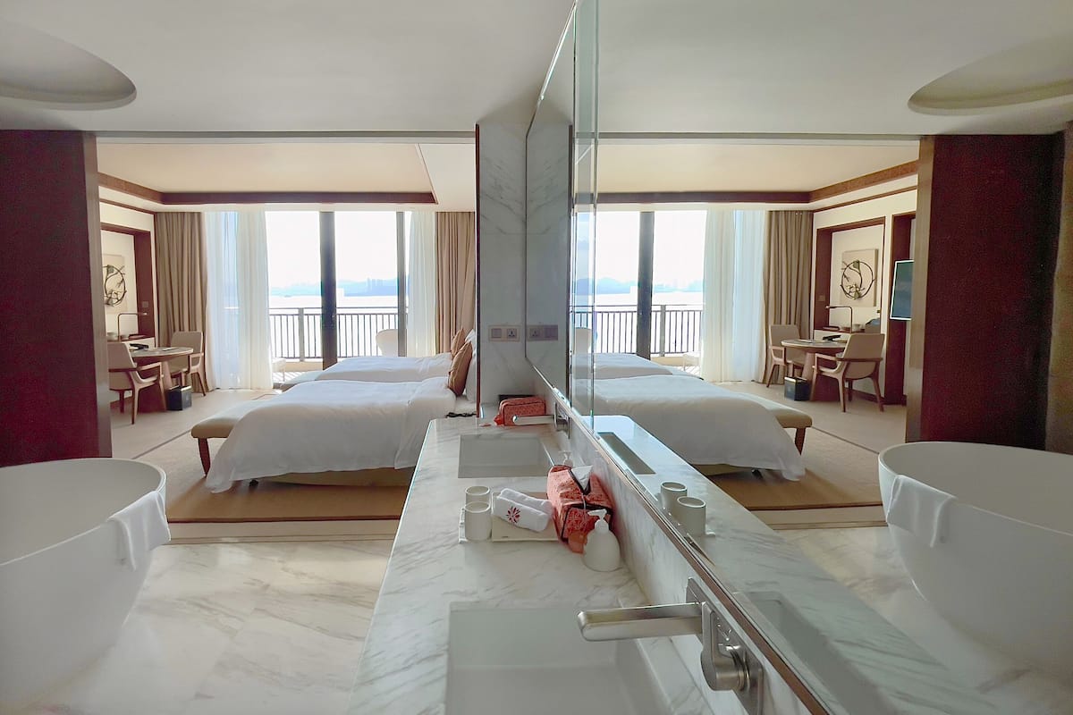 Une chambre d’hôtel avec deux lits, un grand miroir, un bureau et une vue sur la mer.