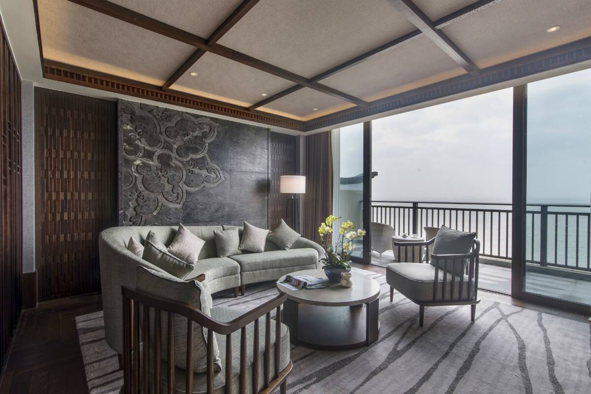 Un salon moderne comprenant un canapé, des fauteuils, une table basse et une grande fenêtre donnant sur une étendue d’eau.