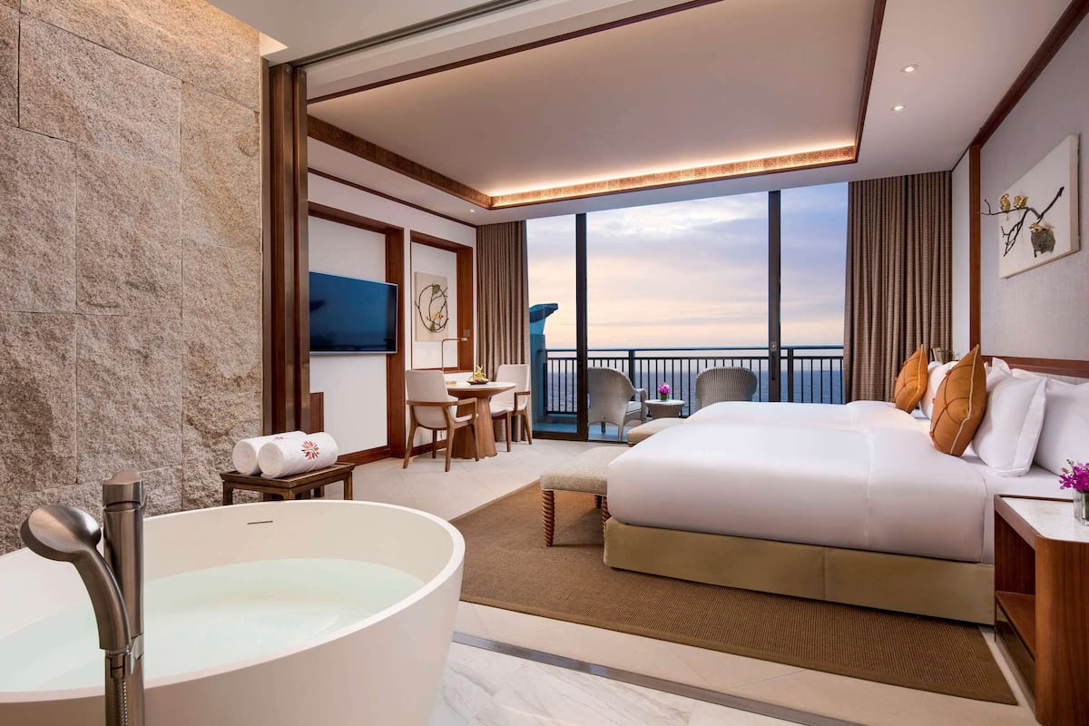 Une chambre d’hôtel moderne dotée d’un grand lit, d’une baignoire, d’un coin repas et d’un balcon offrant une vue sur la mer.