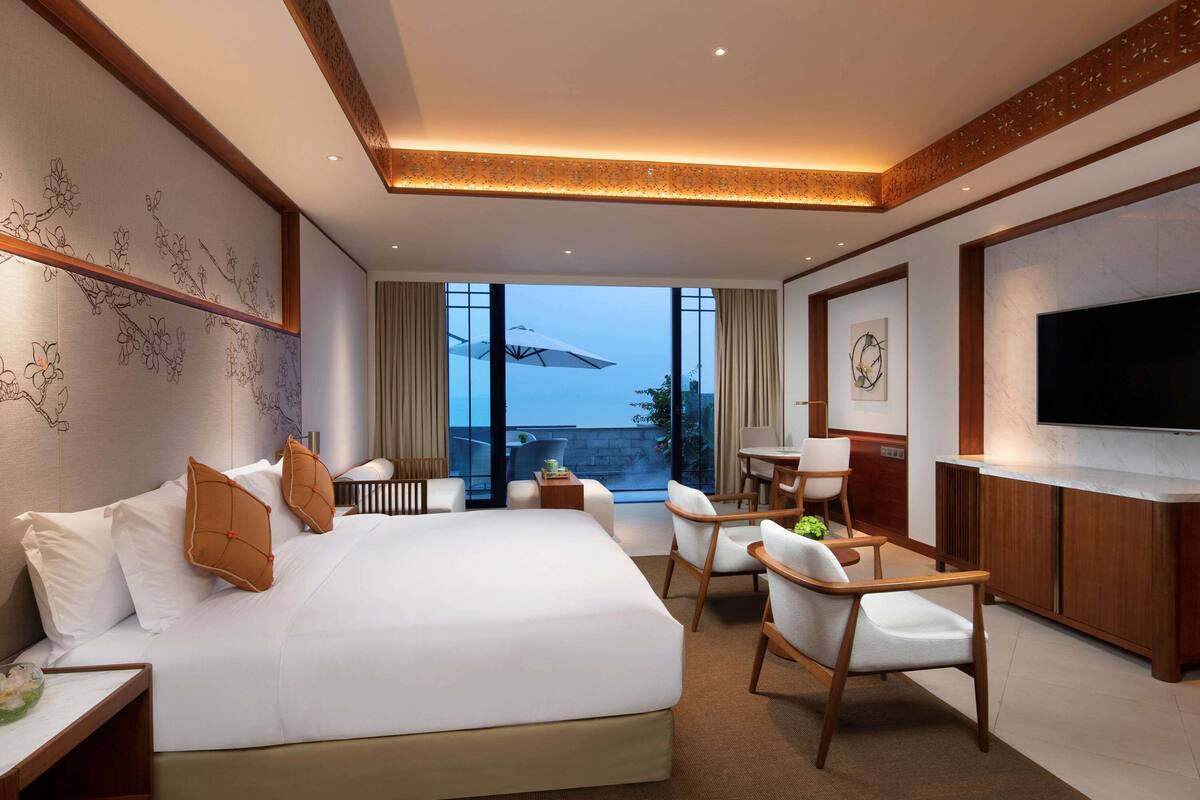 Une chambre d’hôtel moderne dotée d’un grand lit, d’un bureau, d’une chaise, d’une télévision et d’un balcon avec vue.