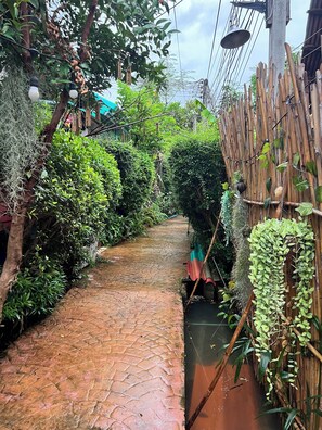 A narrow brick pathway flanked by lush greenery and bamboo structures.