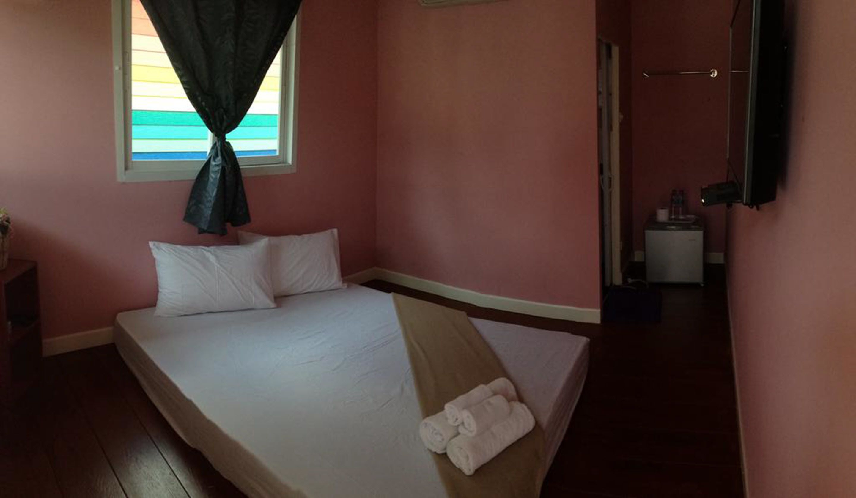 A single bed with white linens and pillows, a window with a curtain, a bedside table, and a mirror on the wall.
