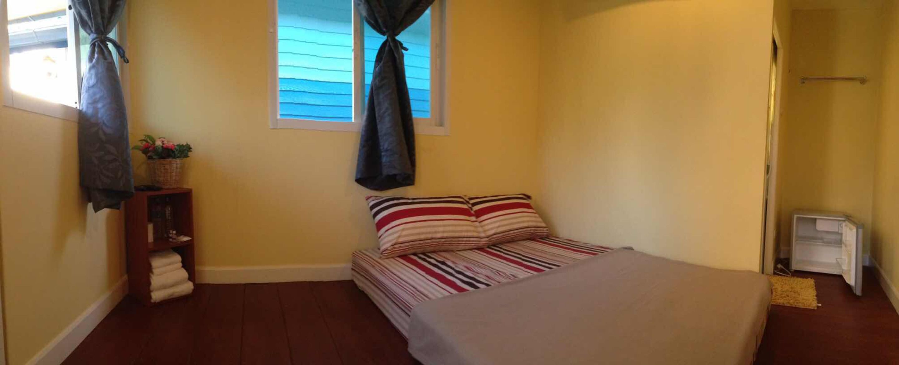 A bedroom with a bed, pillows, a nightstand, a window with curtains, and a radiator.