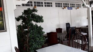 A covered outdoor seating area with a white wall, ceiling fan, and potted plants. - Se Sun Amphawa (Amphawa)