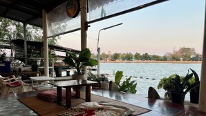 A room with a view of a lake, a table with a cushion, and potted plants. - Se Sun Amphawa (Amphawa)