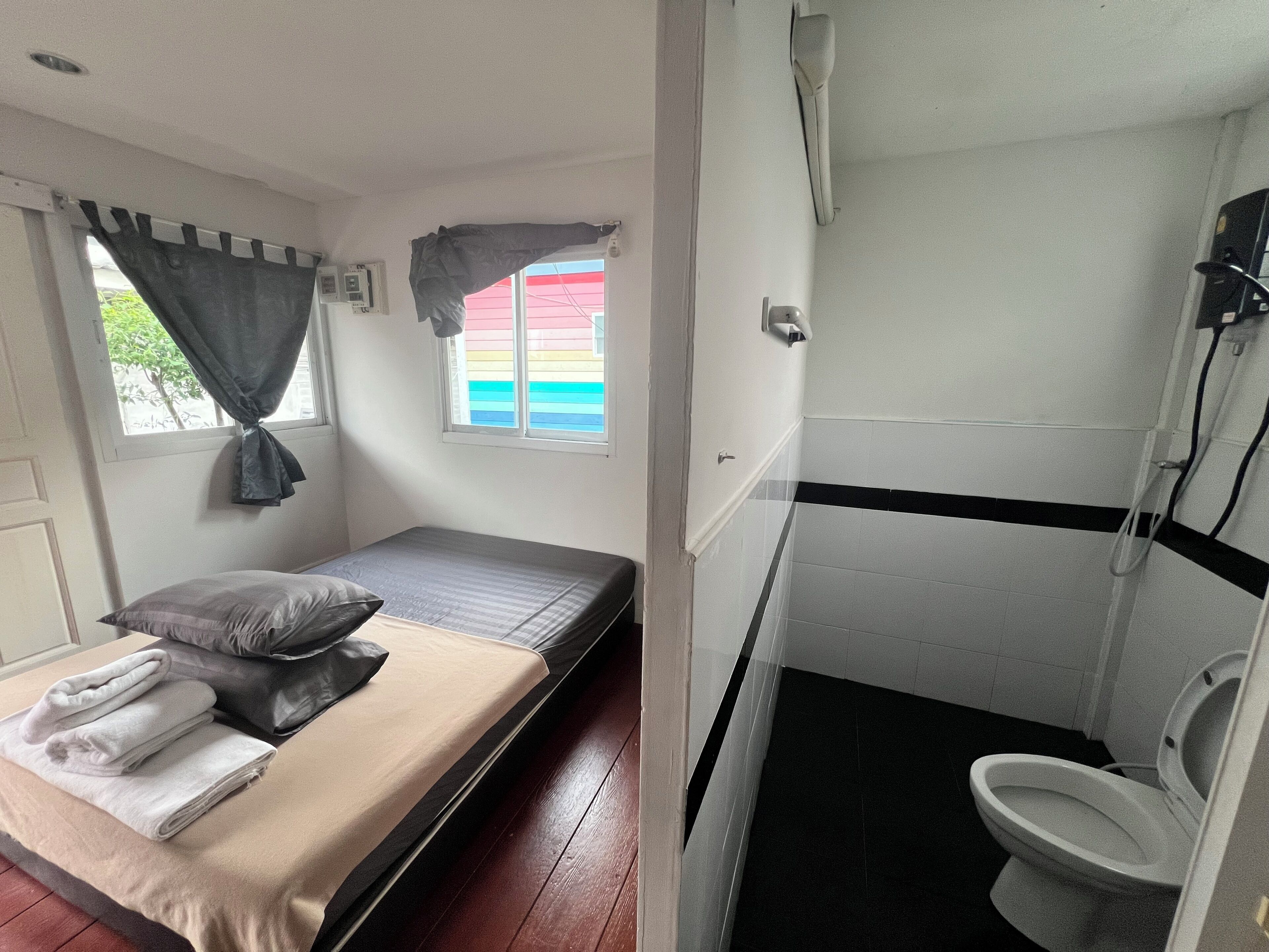 A small, single-room accommodation with a bed, a window with curtains, a bathroom with a toilet, and a shower.