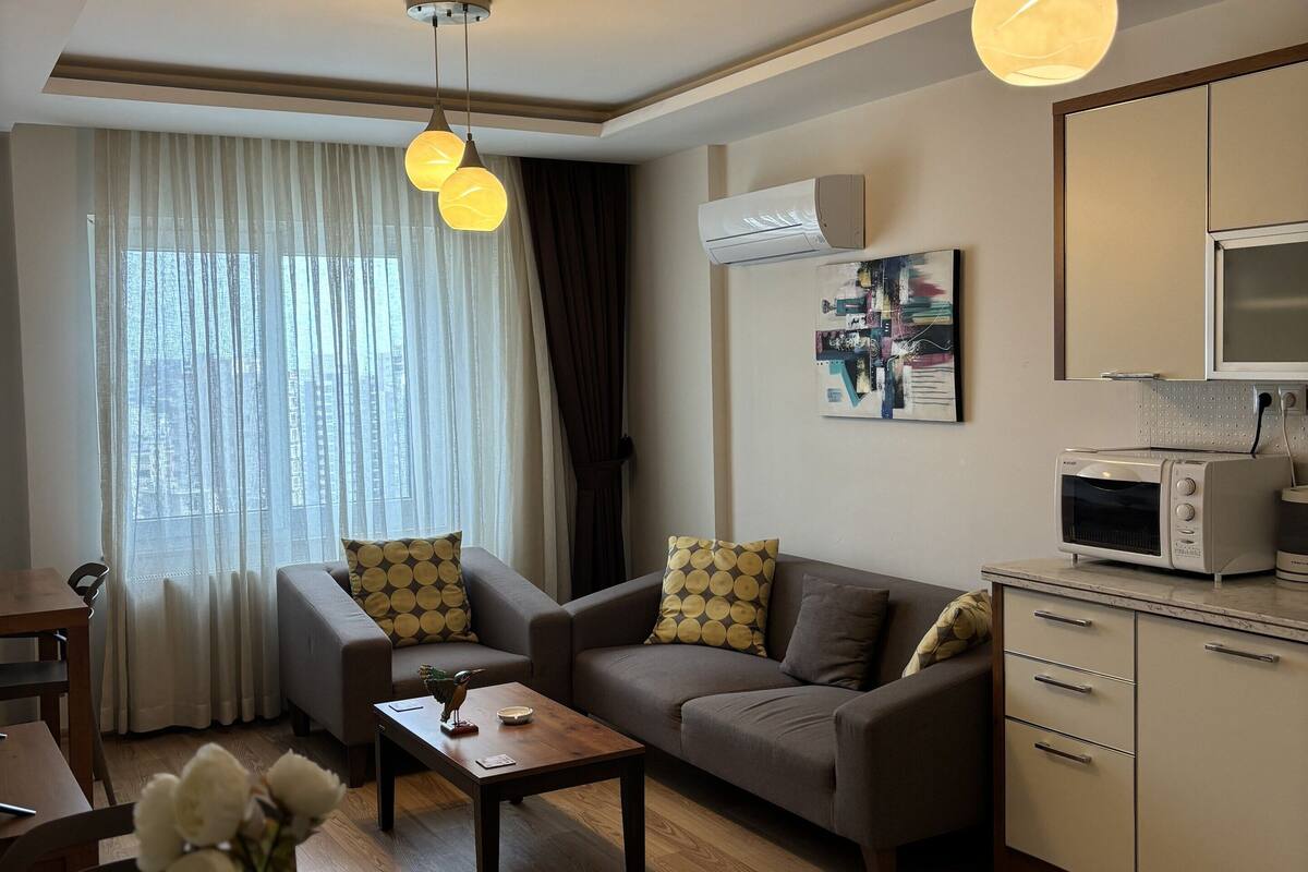 A modern living room with a sofa, coffee table, and a dining area with a table and chairs. There is a kitchen area with a microwave and cabinets.