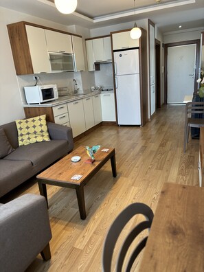 A compact living space with a kitchenette, a sofa, a wooden coffee table, and a dining area with chairs. - Upart Home (Mersin)